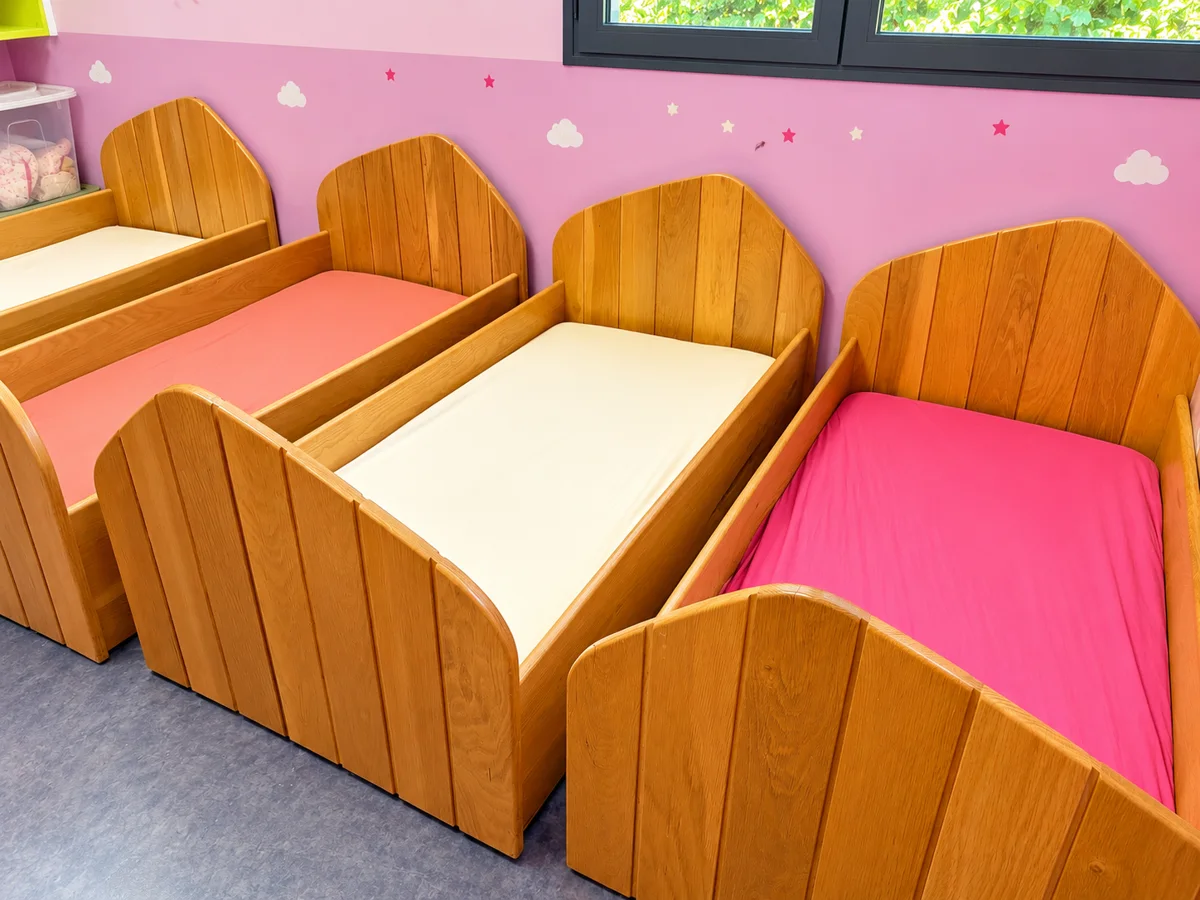 Espace repos de Bonbon aux murs roses décorés de nuages, avec des lits bas en bois aux draps rose et blanc
