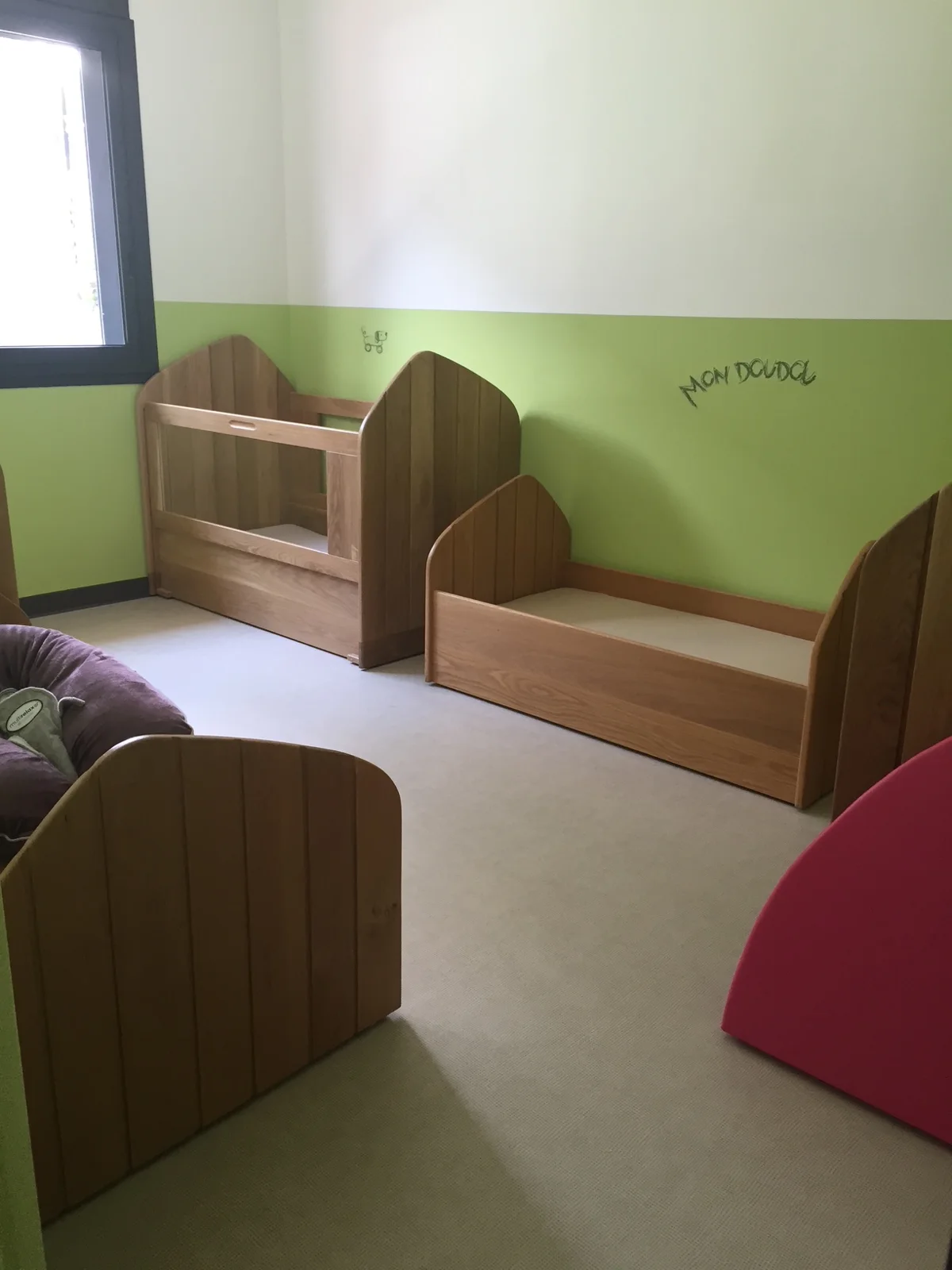 Espace repos de Caramel aux murs vert tendre, avec lits bas en bois et inscription « Mon doudou » au mur