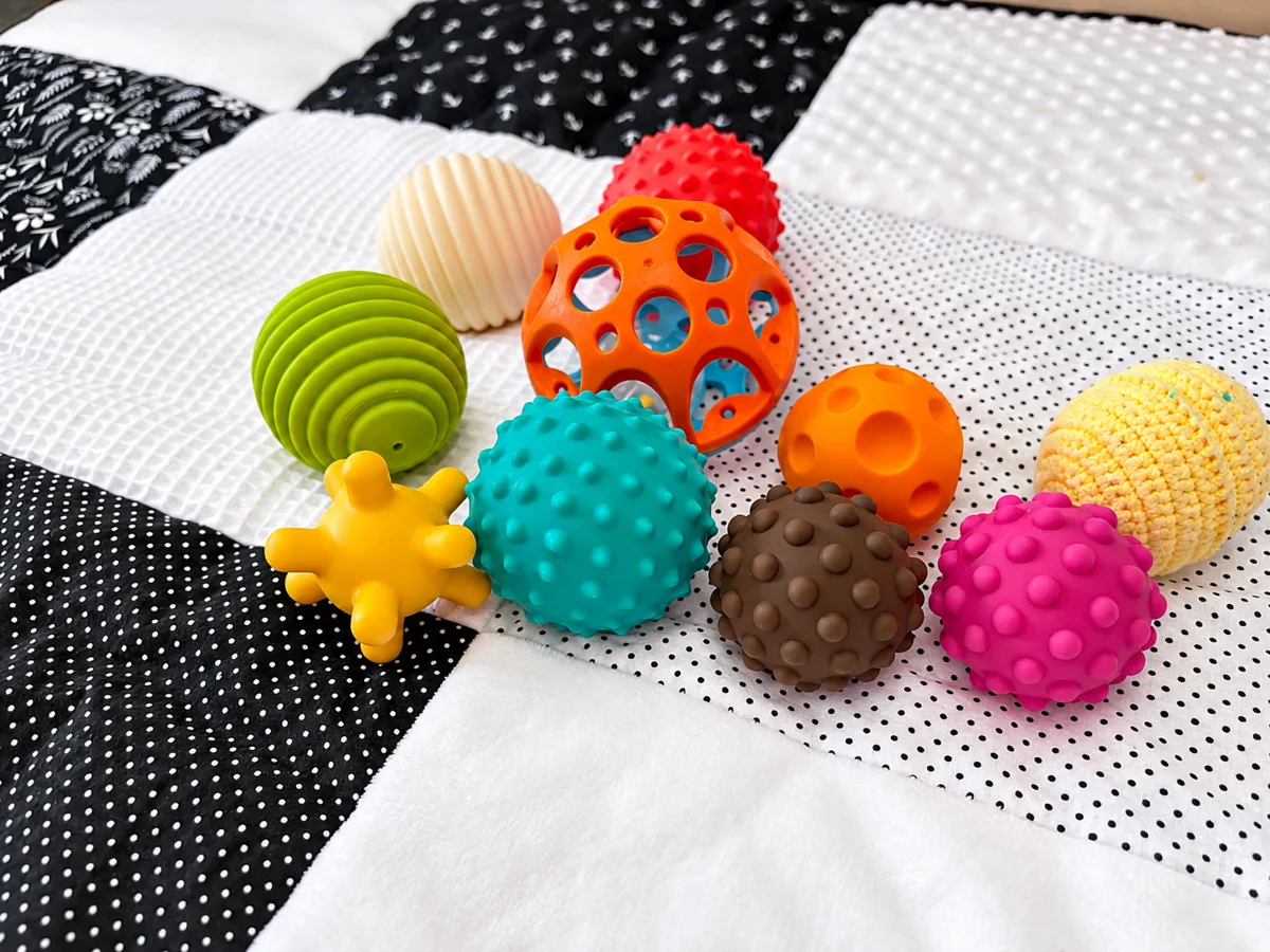 Balles sensorielles à picots et à reliefs de toutes les couleurs sur un tapis d’éveil noir et blanc, chez Chocolat