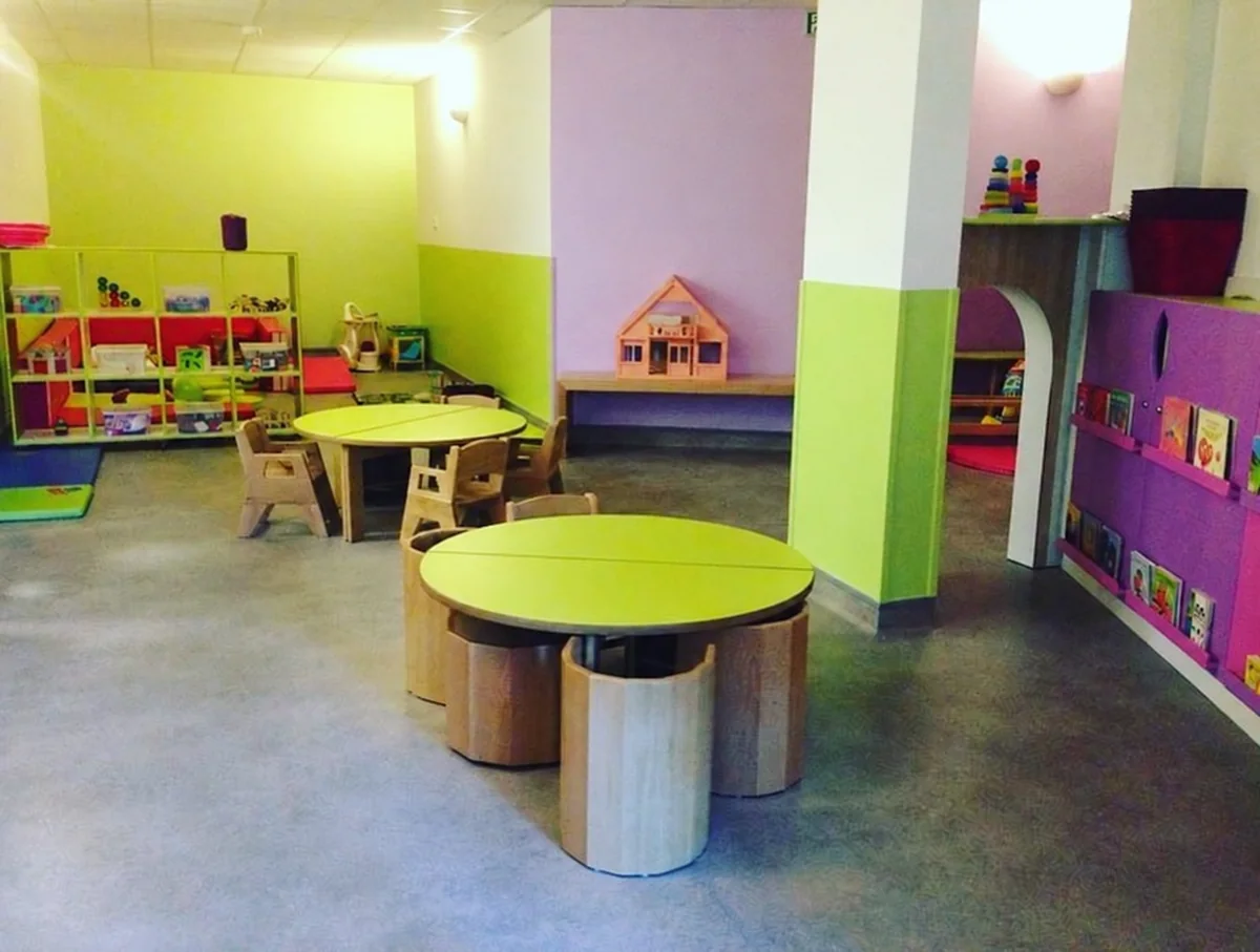 Salle de vie de la micro-crèche Les Makis à Boucan Canot, aux murs vert anis et mauve, avec tables rondes en bois et étagères de jeux