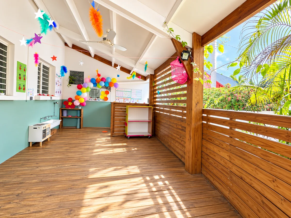 Terrasse couverte des Suricates, plancher en bois ensoleillé, cuisinette de jeu et ballons colorés au mur