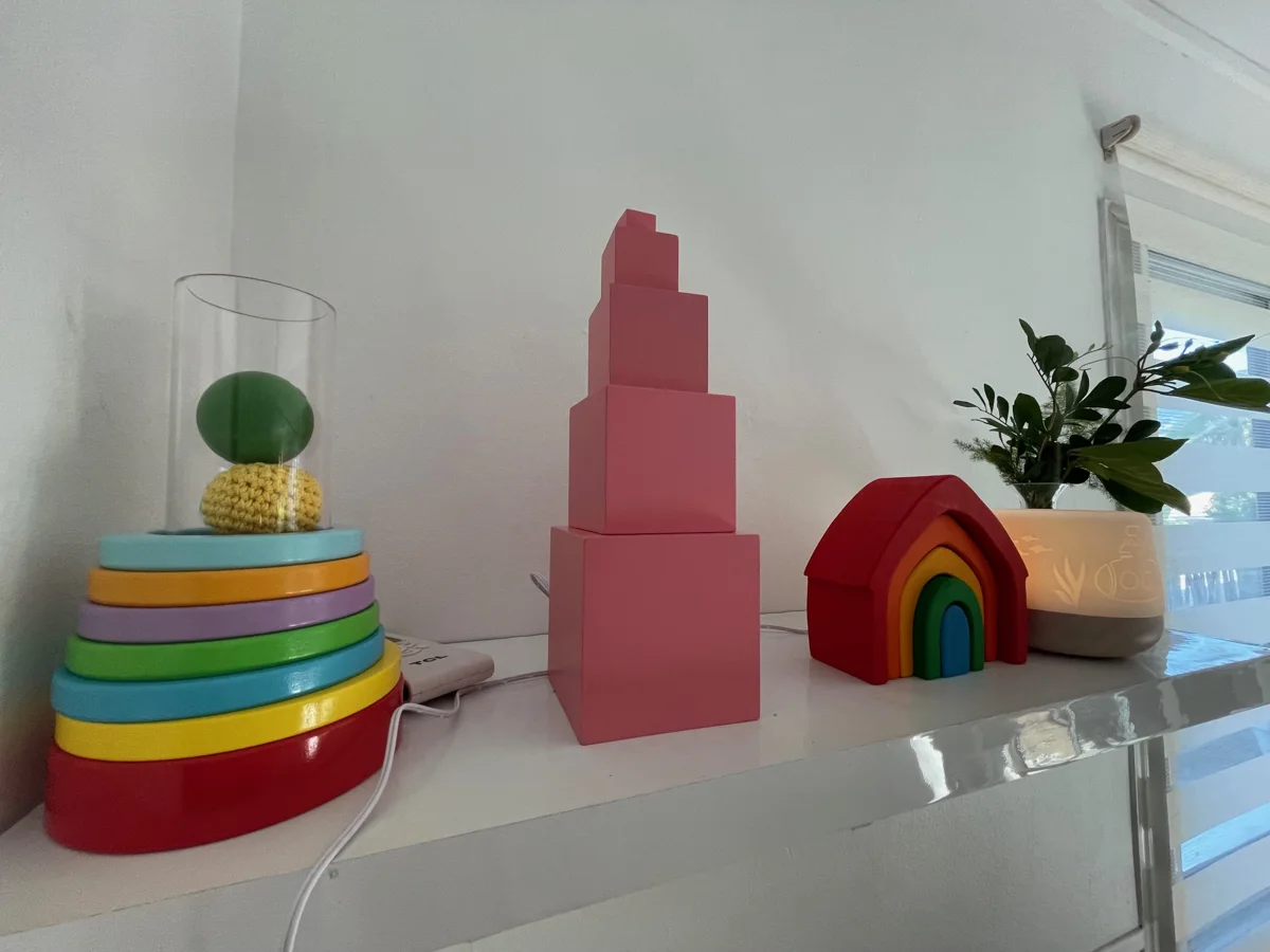 Tour rose, anneaux à empiler et arc-en-ciel en bois posés sur une étagère blanche chez Pitchou