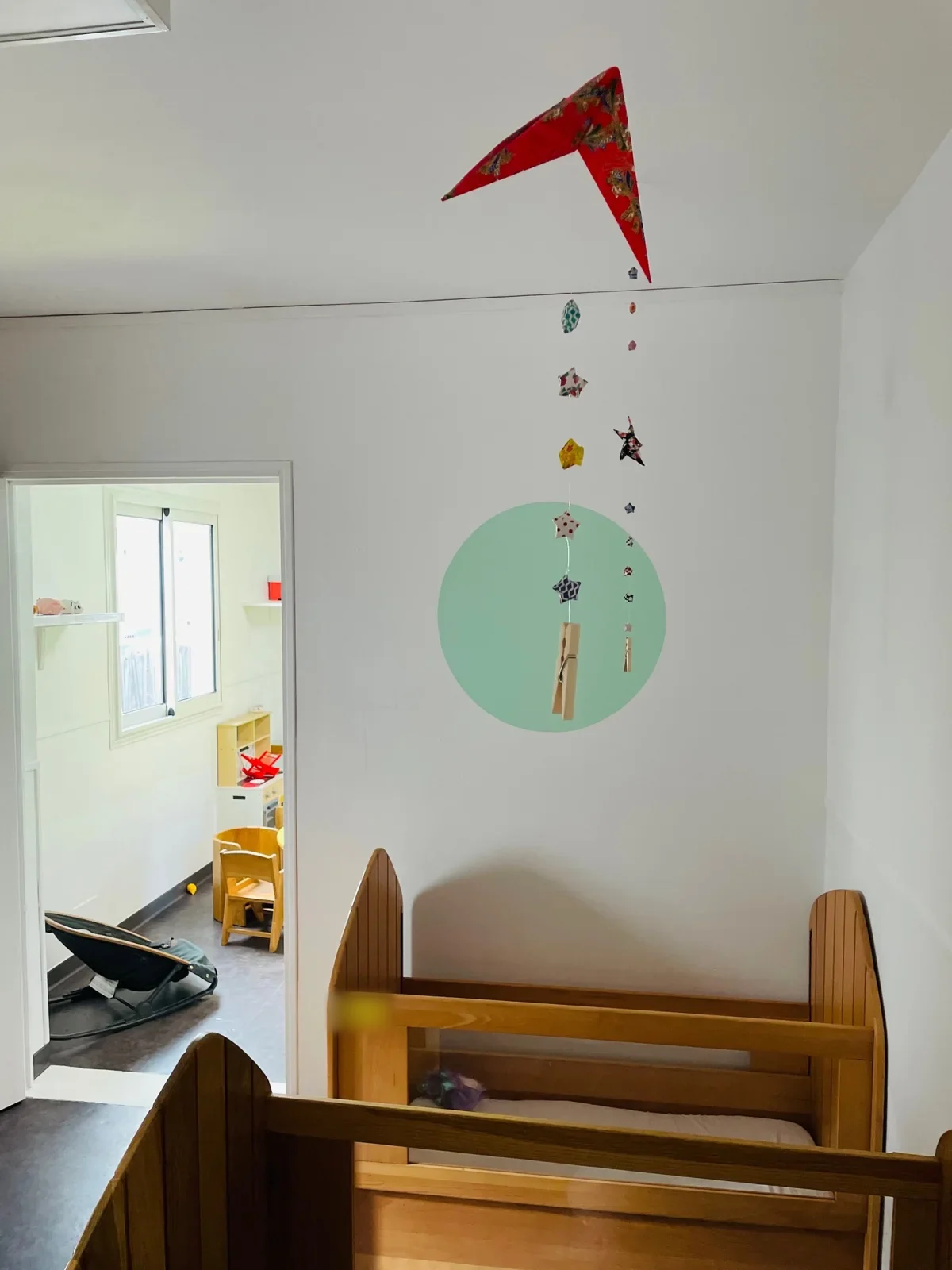 Espace repos de Pitchou avec un lit à barreaux en bois sous un mobile d’origami suspendu